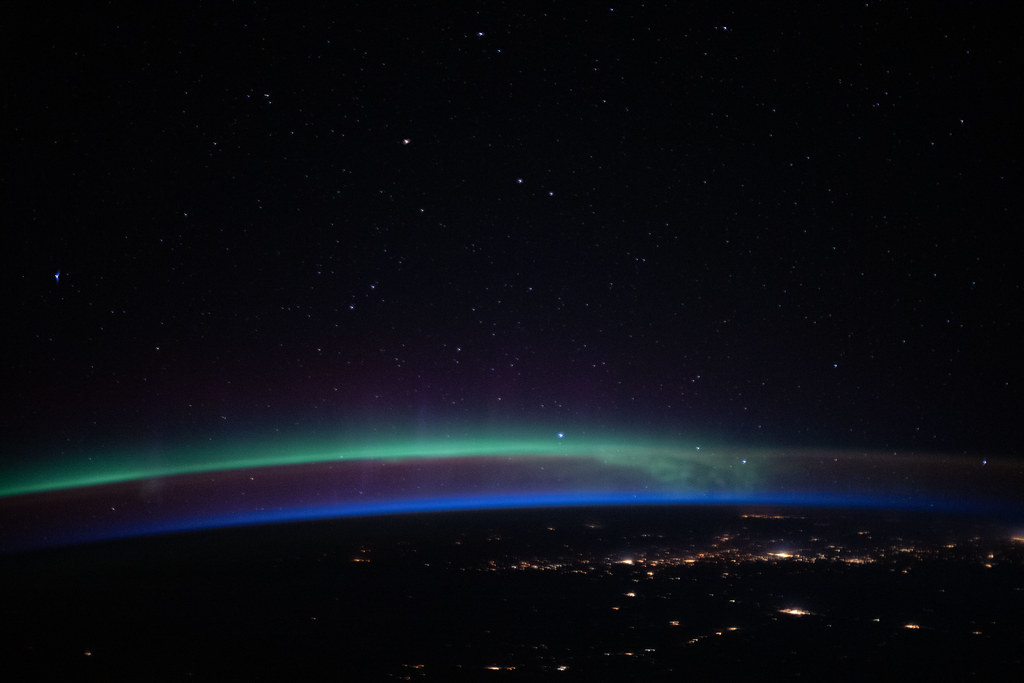 An aurora above the city lights and a beneath a starry sky